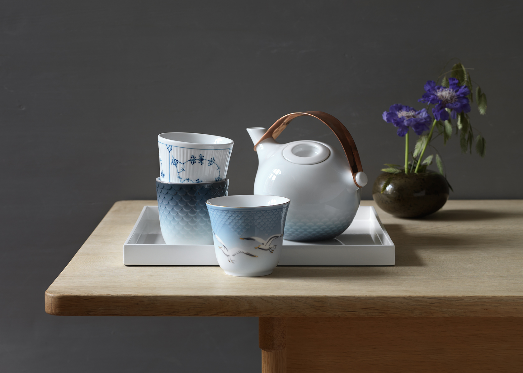 The Seagull Thermal Mug standing in front of a tray with other Royal Copenhagen Thermal Mugs and the HAV Teapot